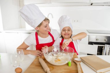 genç anne ve küçük tatlı kızı aşçı şapkası ve birlikte evde mutfak pişirme yemek önlük