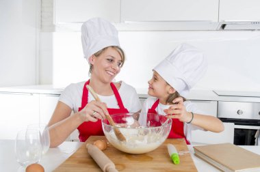 genç anne ve küçük tatlı kızı aşçı şapkası ve birlikte evde mutfak pişirme yemek önlük