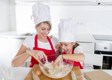genç anne ve küçük tatlı kızı aşçı şapkası ve birlikte evde mutfak pişirme yemek önlük