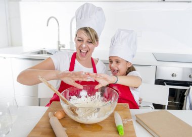 genç anne ve küçük tatlı kızı aşçı şapkası ve birlikte evde mutfak pişirme yemek önlük