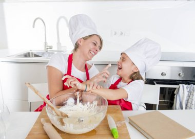 genç anne ve küçük tatlı kızı aşçı şapkası ve birlikte evde mutfak pişirme yemek önlük