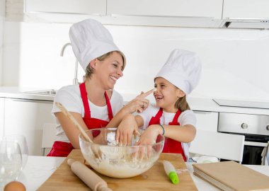 genç anne ve küçük tatlı kızı aşçı şapkası ve birlikte evde mutfak pişirme yemek önlük