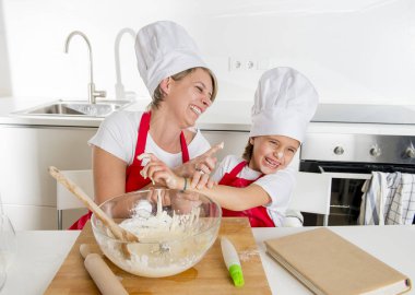 genç anne ve küçük tatlı kızı aşçı şapkası ve birlikte evde mutfak pişirme yemek önlük