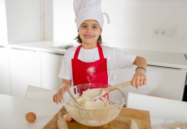 Mini şef aşçı şapkası ve un ve tatlı çöl mutlu gülümseyen hazırlama pişirme yumurta karıştırma önlük kızla