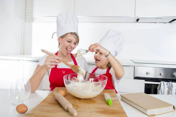 Young mother and little sweet daughter in cook hat and apron cooking together baking at home kitchen — Stock Photo, Image