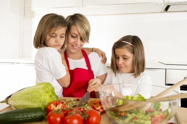 年轻的母亲在厨师围裙和烹饪一起准备沙拉的甜美漂亮的双胞胎女儿 — 图库照片