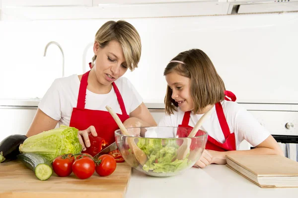 Madre e hija pequeña cocinando junto con delantal cocinero preparando ensalada en la cocina casera — Foto de Stock
