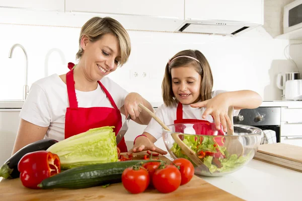 Mãe e pequena filha cozinhar em conjunto com avental de cozinha preparando salada em casa cozinha — Fotografia de Stock