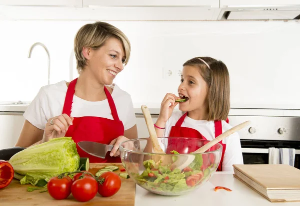 Mãe e pequena filha cozinhar em conjunto com avental de cozinha preparando salada em casa cozinha — Fotografia de Stock