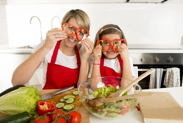 Mãe e pequena filha cozinhar em conjunto com avental de cozinha preparando salada em casa cozinha — Fotografia de Stock