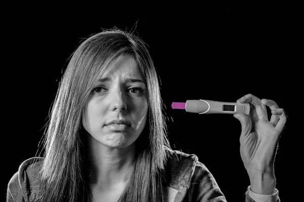 Young sad pregnant woman or female teenager scared and shocked holding pregnancy test positive result — Stock Photo, Image