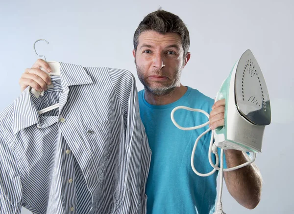 Ung attraktiv och frustrerad man håller järn och skjorta stressad och trött i uttråkad och lata ansikte — Stockfoto