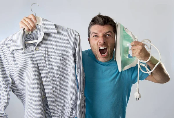 Jovem atraente e frustrado homem segurando ferro e camisa estressado e cansado no rosto entediado e preguiçoso — Fotografia de Stock