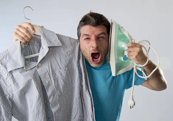 Joven atractivo y frustrado hombre sosteniendo hierro y camisa estresado y cansado en la cara aburrida y perezosa — Foto de Stock