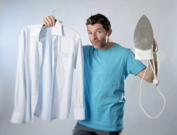 Aantrekkelijk en tevreden jongeman holding ijzer en slick shirt lacht vrolijk en eigenwijs — Stockfoto