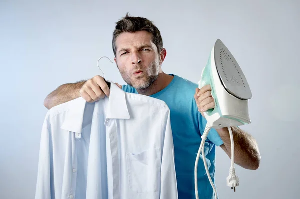 Young attractive and satisfied man holding iron and slick shirt smiling happy and cocky — Stock Photo, Image