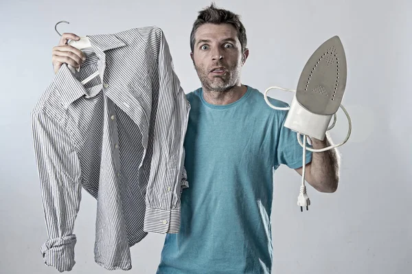 Joven atractivo y frustrado hombre sosteniendo hierro y camisa estresado y cansado en la cara aburrida y perezosa — Foto de Stock