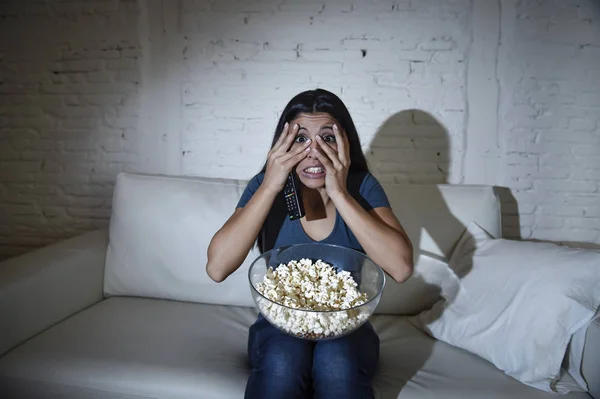 Latinsk kvinna på hem soffa soffa i vardagsrummet framför TV som täcker ögon förskräckt — Stockfoto