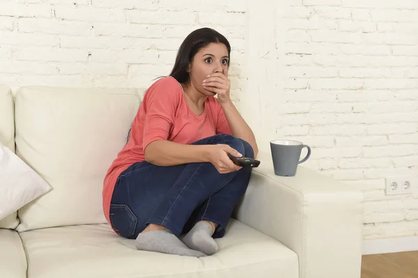 Mujer latina sentada en casa sofá sofá en la sala de estar viendo la televisión miedo película de terror —  Fotos de Stock