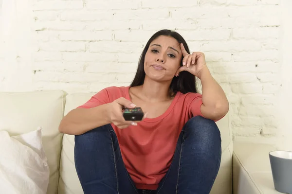Латиноамериканка, сидящая дома на диване в гостиной и смотрящая телевизор усталый и скучный — стоковое фото