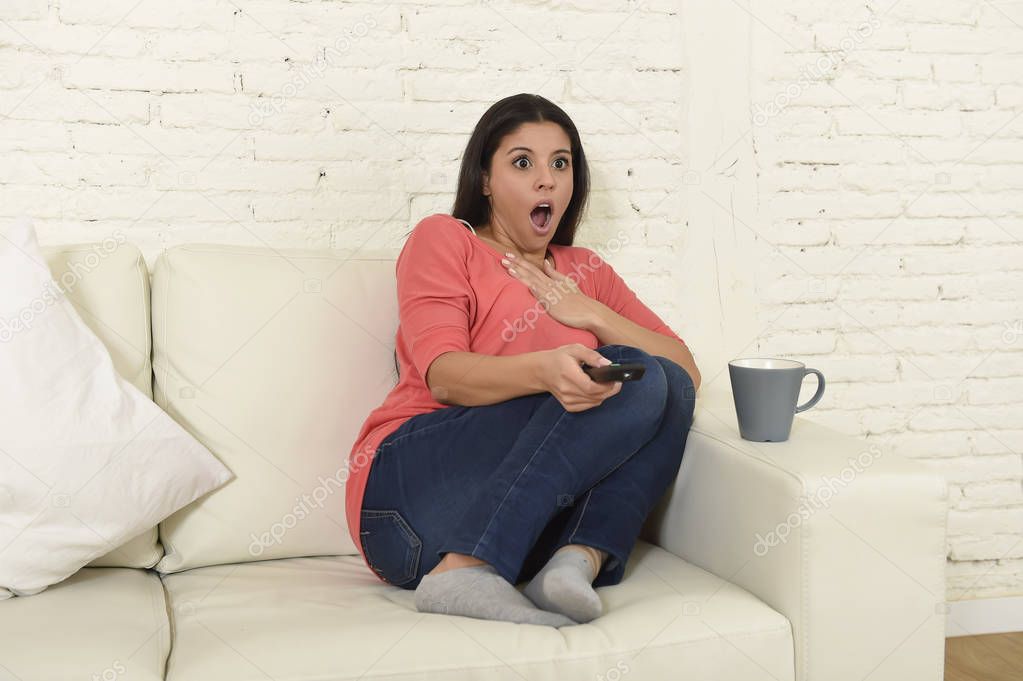  latin woman sitting at home sofa couch in living room watching television scary horror movie