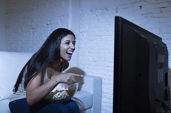 Счастливая женщина, смотрящая телевизор на диване, с удовольствием ест кукурузу — стоковое фото