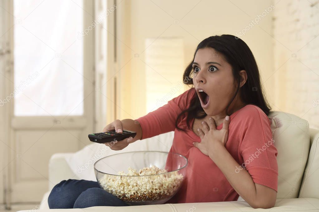  latin woman sitting at home sofa couch in living room watching television scary horror movie
