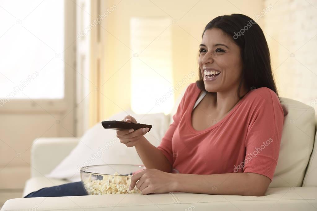 attractive latin woman at home sofa couch laughing and smiling happy watching television 