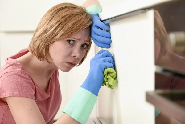 Женщина на кухне с резиновыми перчатками ткани и моющего средства уборка скучно и устал — стоковое фото