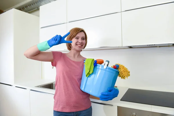 Mujer feliz en guantes sosteniendo cubo de limpieza con tela y hogar — Foto de Stock