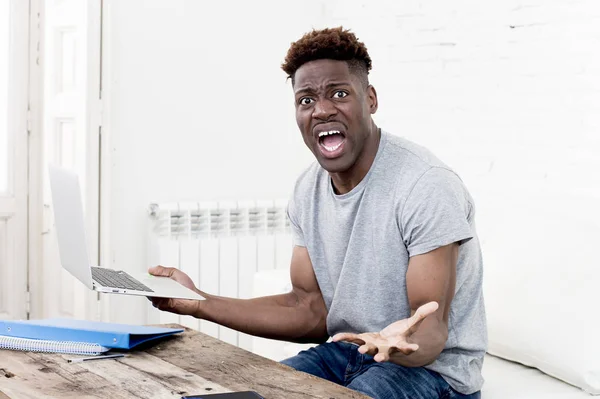 Afrikanisch-amerikanischer Mann sitzt zu Hause im Wohnzimmer und arbeitet mit Laptop und Papierkram — Stockfoto