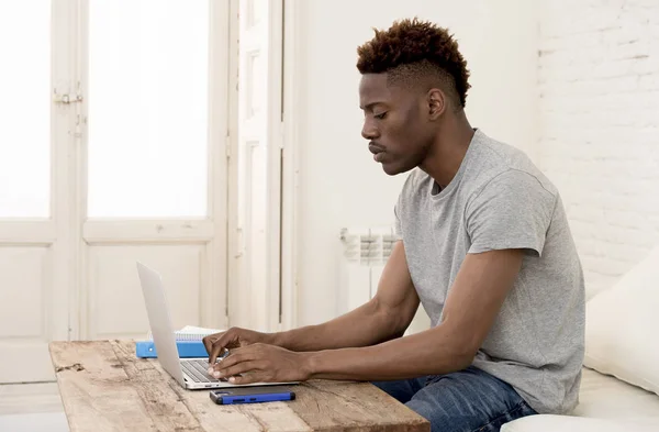 Afro-Amerikaanse man zit thuis woonkamer werken met laptopcomputer en papierwerk — Stockfoto