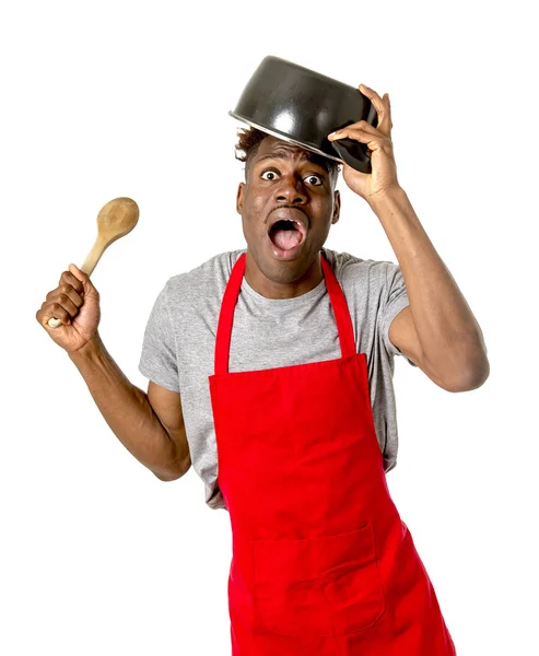 Confuso hombre afroamericano negro en delantal de chef sosteniendo olla en su cabeza — Foto de Stock