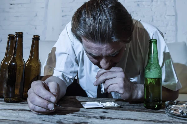 Homem alcoólatra e drogado desperdiçado com gravata solta roncando cocaína e bebendo garrafas de cerveja em casa — Fotografia de Stock