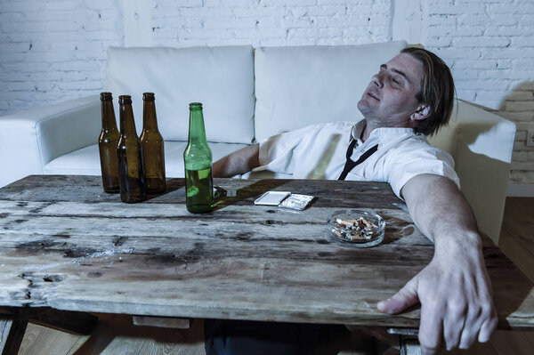 wasted alcoholic and drug addict man with loose tie snorting cocaine and drinking beer bottles at home 