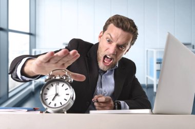 angry exploited businessman at office desk stressed and frustrated with computer laptop and alarm clock clipart