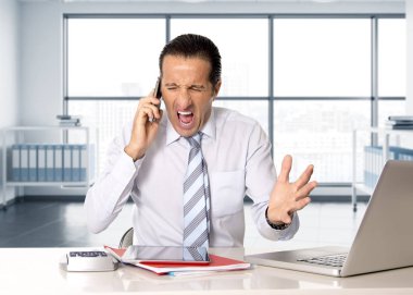 kızgın üst düzey iş adamı çalışma ve bilgisayar masasında cep telefonu üzerinde konuşurken stres