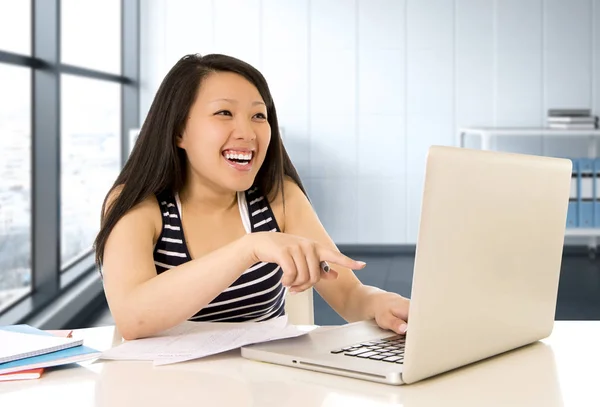 Happy chinese asian woman working and studying on her computer sitting at modern office desk smiling cheerful — Stock Photo, Image