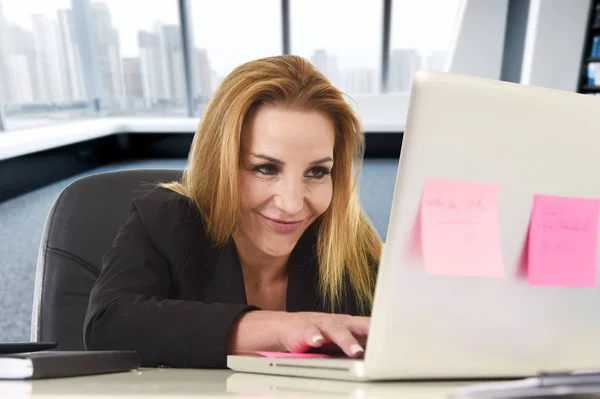 Détendue femme des années 40 avec les cheveux blonds souriant confiant assis sur une chaise de bureau travaillant à l'ordinateur portable — Photo