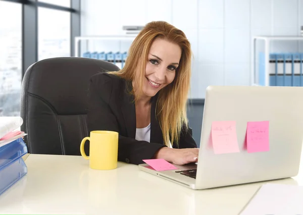 40 代をリラックスして自信を持ってラップトップ コンピューターで作業するオフィスの椅子に座って笑っているブロンドの髪を持つ女性 — ストック写真