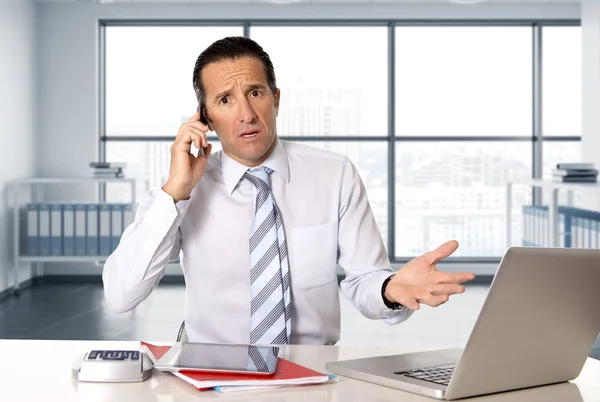 Enojado hombre de negocios senior en el estrés trabajando y hablando en el teléfono móvil en el escritorio de la computadora — Foto de Stock