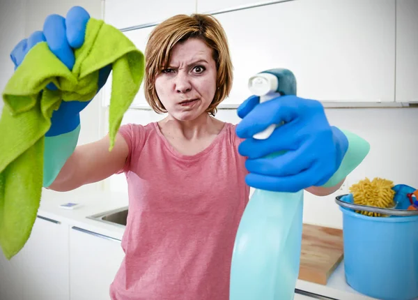 Woman at home kitchen in gloves holding cleaning scourer and detergent spray bottle rubbing with cloth — Stock Photo, Image