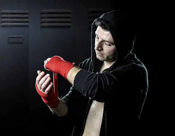 Man in boxing hoodie jumper with hood on head wrapping hands and wrists getting ready for fighting — Stock Photo, Image