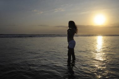 Su özgür ve rahat Bali sunset beach ufukta bakarak üzerinde duran genç güzel Asyalı kadın silüeti