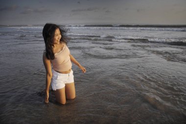 özgür ve mutlu Bali Adası, Endonezya kumsalda diz çökmüş olarak günbatımı Plajı'nda eğleniyor gülümseyen genç güzel Asyalı kadın