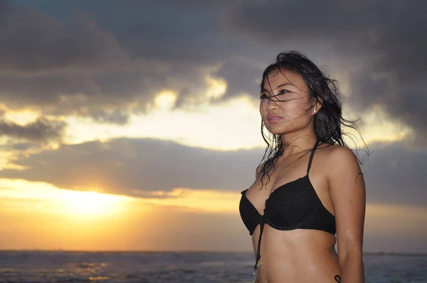 Mladá, krásná a sexy Asijské žena v černé bikiny uvolněně bavit v sunset beach Bali ostrov Indonésie — Stock fotografie