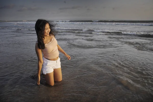 Young beautiful asian woman smiling free and happy having fun at sunset beach in Bali island of Indonesia kneeling on sand — Stock Photo, Image