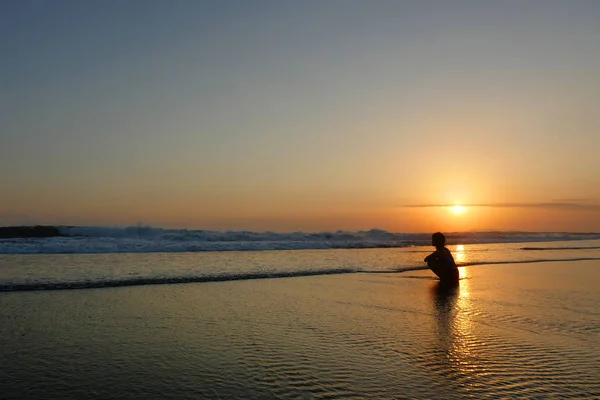 年轻美丽亚洲女孩独自在海边看着橙色的天空日落越过海洋 — 图库照片