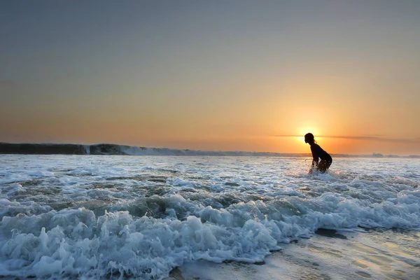 Young beautiful Asian girl alone at sea shore looking at orange sky sunset over ocean — Stock Photo, Image