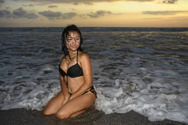 Sexy a krásná mladá asijská žena relaxační hravé na sunset beach klečí na vodě — Stock fotografie
